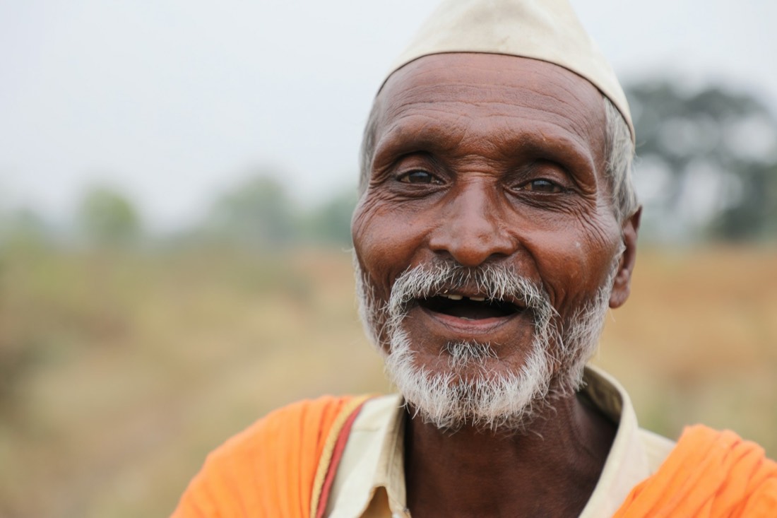 A smiling Indian farmer in a white cap